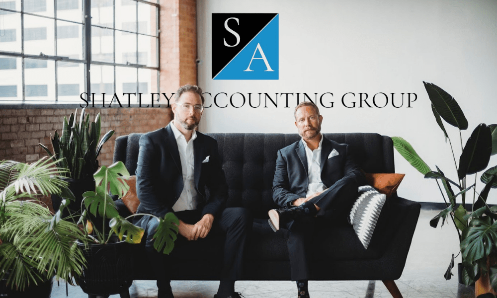 Two men in suits sit on a black sofa with plants around. "Shatley Accounting Group" is displayed with a blue and black SA logo above them.